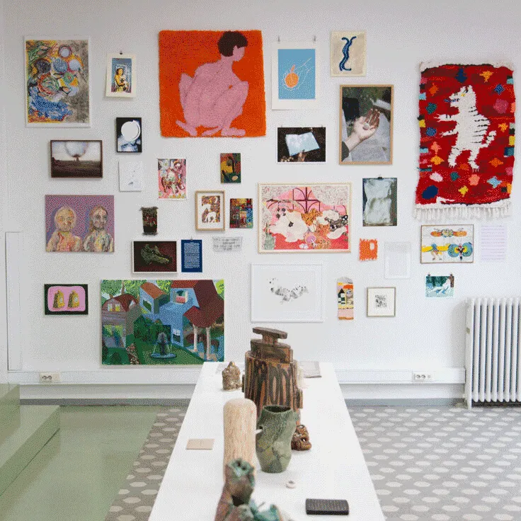 a white wall in a gallery spaced filled with artworks by various artists 
                        ranging in size and media.
