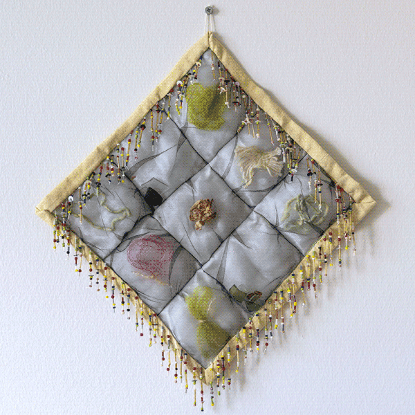 A small and square puffy quilt. Each puffed block contains an item. 
                    The binding is a pale yellow and border is decorated with beaded fringe.