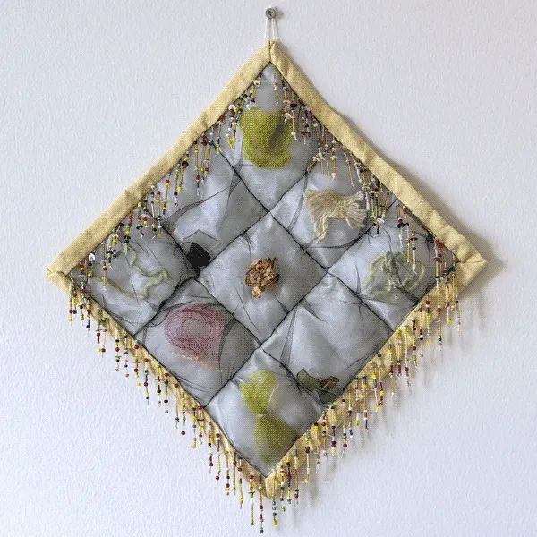 A small and square puffy quilt. Each puffed block contains an item. 
                            The binding is a pale yellow and border is decorated with beaded fringe.
