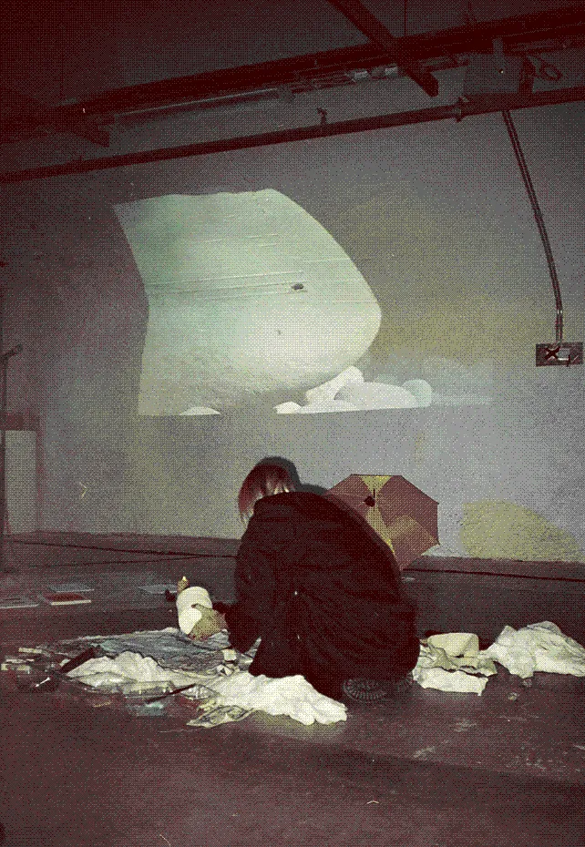 Elina Nissinen is crouching on the floor while holding a ball of thread. Around her are trays of paint and fabric.