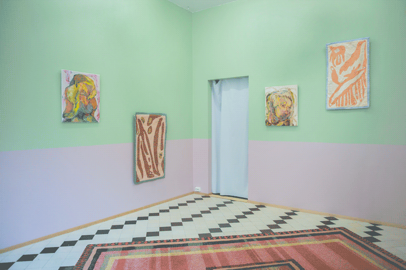 The same space, but from a different angle. From left to right, on the wall 
                there is: the yellow painting, the brown quilt, a brown paintinh of a human-like
                figure and a small pink quily with organic shapes. 