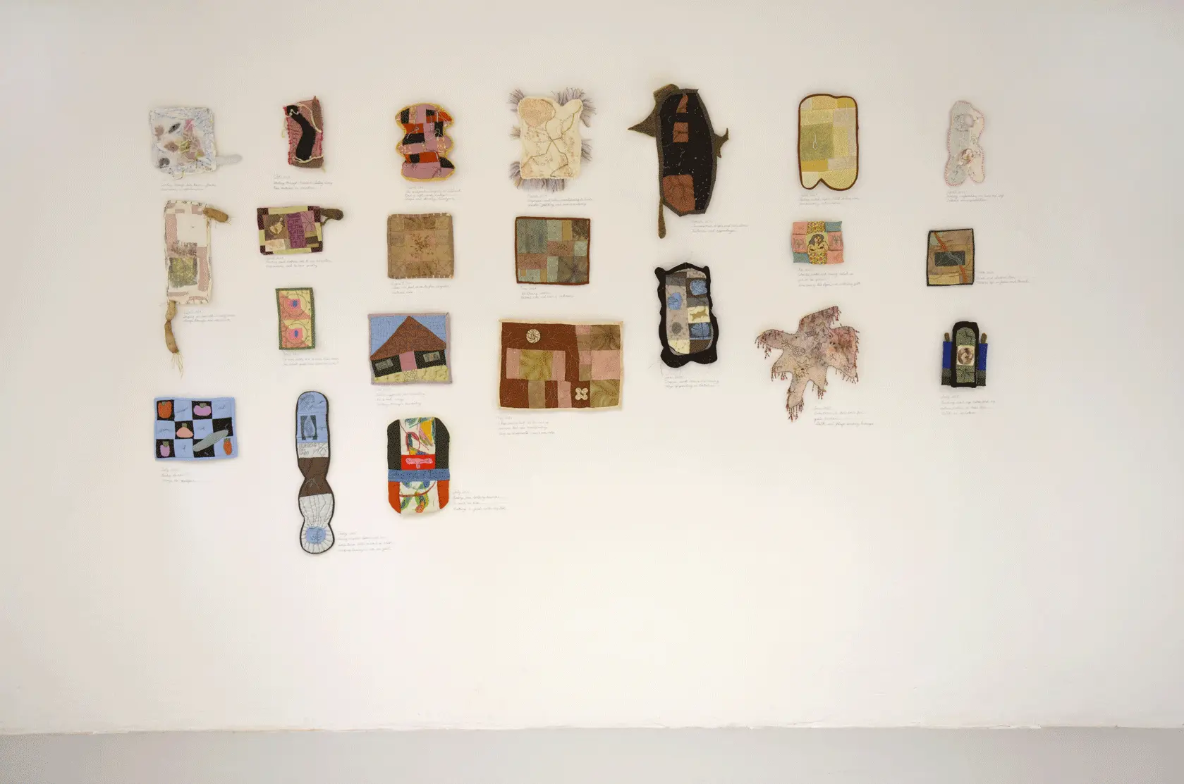 A close up of the mentioned quilts on the wall. 
                    There are four rows and seven colums of small quilts.