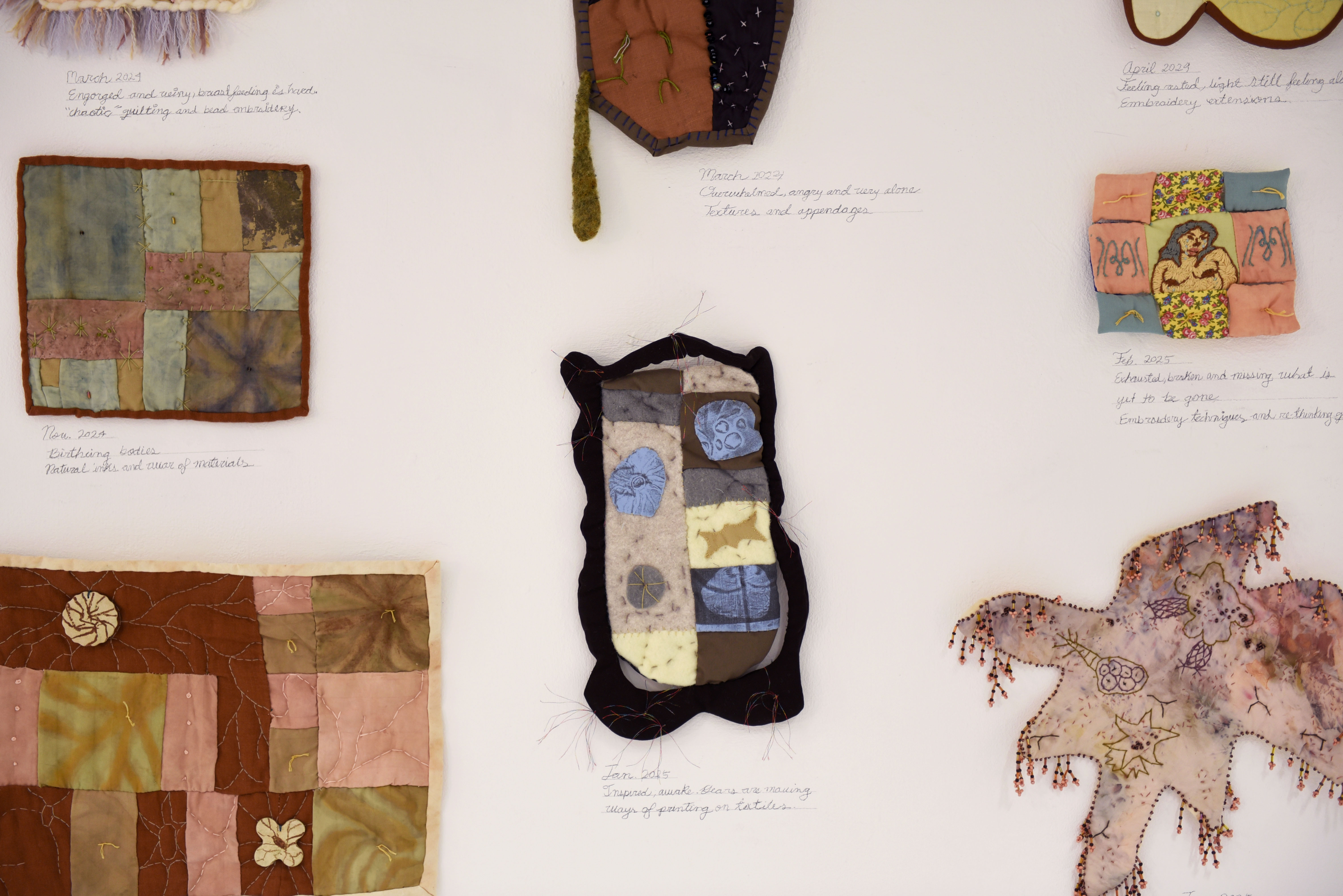 An even closer look at the quilts on the wall.
                    Smaller details are visible now and below each quilt is a hand-written 
                    note from the artists, sharing the date it was made and a memory or 
                    feeling tied to each work.