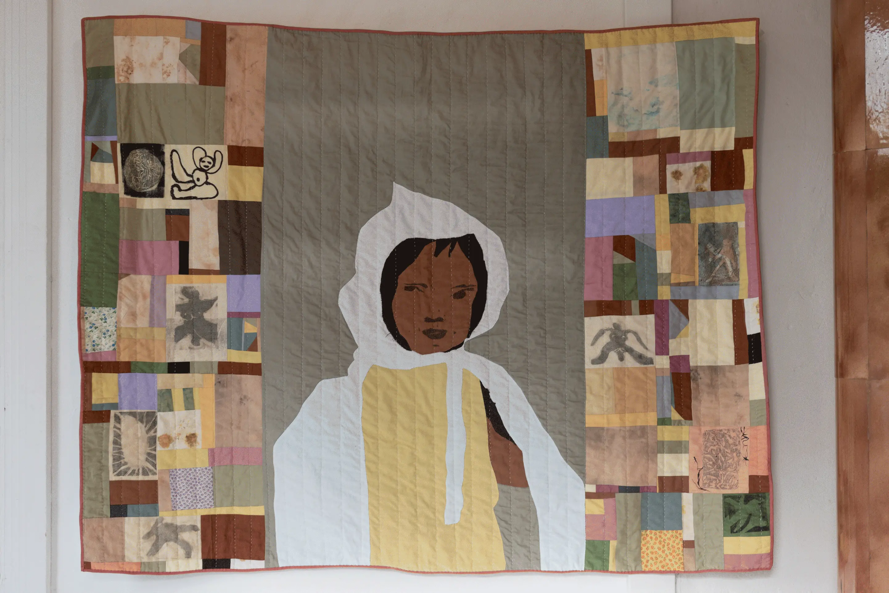 A close up of the quilt with the small child wearing a white cape